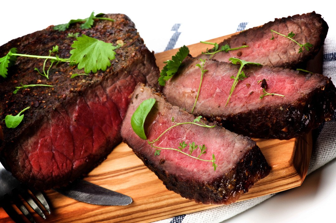 Sliced delicious roast beef medium rare on wooden cutting board fork and table knife closeup