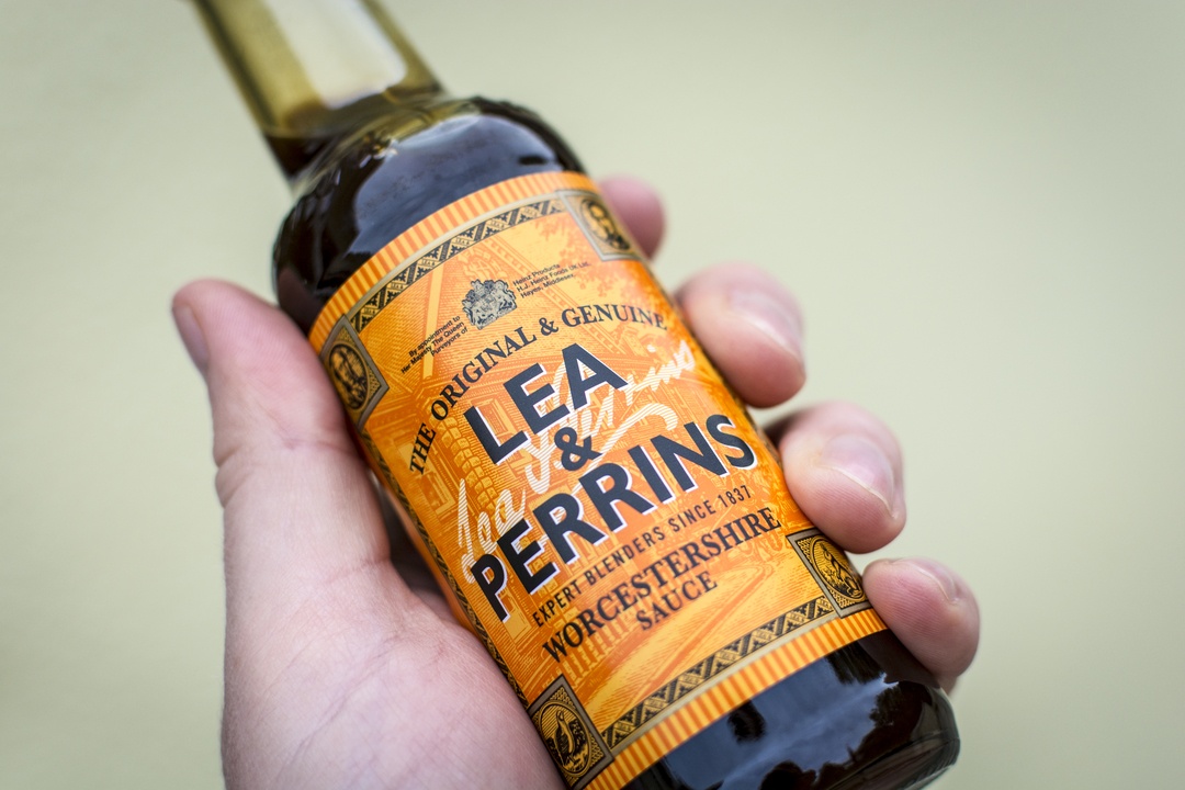 Close up of a male hand holding a bottle of Lea & Perrins Worcestershire Sauce - a popular condiment / cooking ingredient.